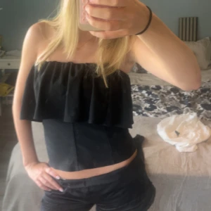 Svart Zara topp med volang  - 😇Högt pris då ja är osäker om ja vill sälja .😇Säljer en svart bandeau tubtopp med bred volang upptill. Toppen är axelbandslös och har en tight passform som framhäver midjan. Perfekt för dig som vill ha en stilren och trendig look. Materialet känns mjukt och följsamt.