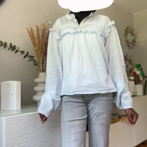Ljusblå blus med volangdetaljer - Säljer en ljusblå blus med volangdetaljer och långa puffiga ärmar. Luftig och skön passform, perfekt för sommaren. Skulle säga att den sitter som en xs då den är i största barnstorlek.