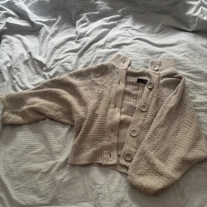 Blå  stickad kofta med stora knappar - Superfin blå stickad kofta med stora knappar framtill och bred ribbad kant. Koftan har en croppad passform och långa ärmar, perfekt att slänga över en topp för en chill look.