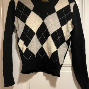 Argyle stickad tröja - Snygg stickad tröja med klassiskt argylemönster i svart, vitt och grått. V-ringad modell med långa ärmar, perfekt för lager-på-lager. Tillverkad i ull och har en tidlös preppy vibe.