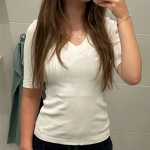 Vit ribbad topp från InWear XS - Säljer en vit ribbad topp från InWear i storlek XS. Toppen har v-ringning och korta ärmar, med en slim passform som sitter snyggt mot kroppen. Materialet är mjukt och stretchigt, perfekt för dig som gillar stilrena och enkla plagg.