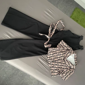 Svart långklänning med mönstrad bälte - Snygg svart långklänning med rund hals och ärmlös design. Till klänningen hör ett beige och svart bälte med grafiskt mönster som matchar den kortärmade skjortan i samma färg och print. Perfekt för dig som gillar stilrena och trendiga looks.