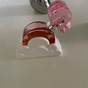 Ariana Grande parfym rosa hjärta - Superfin parfym från Ariana Grande i en rund, rosa glasflaska med hjärtformat lock och vit molnformad hållare. Flaskan har en söt och modern design som verkligen sticker ut på hyllan. 
