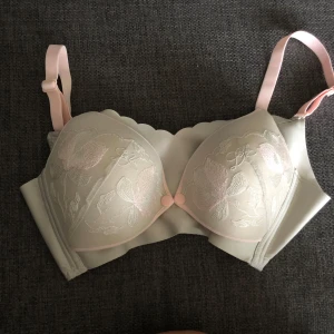 Ljusrosa blommig bh - Supersöt Bh (för amma) i ljusrosa och beige med broderade blommor på kuporna. ! Aldrig använd såklart! Justerbara axelband och knäppning bak. En amningsBH som aldrig är använd. knapp i fram som ni ser på bilden så enkel att använda