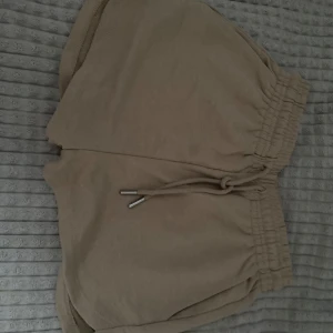 Beige mjuka shorts med snörning - Säljer ett par beiga shorts i mjuk bomull med elastisk midja och snörning framtill. De har en avslappnad passform och rundade benslut, perfekta för chill dagar eller träning. Enkla att matcha och superbekväma.