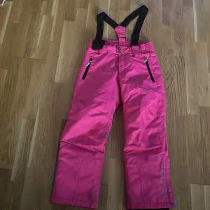Rosa täck/ skid/ vinterbyxor från Wall Ride - Säljer ett par snygga rosa täckbyxor från Wall Ride i storlek 146. Byxorna har svarta hängslen, dragkedjor vid fickorna och reflexdetalj vid benet. Perfekta för vinterns alla äventyr i snön! Vi kan diskutera om priset :)