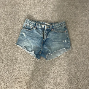 Blå jeansshorts från Perfect Jeans - Snygga blå jeansshorts från Perfect Jeans med rå kant och slitna detaljer. Klassisk femficksmodell, knapp och dragkedja fram samt bälteshällor. Perfekt för dig som gillar en chill och avslappnad stil på sommaren.