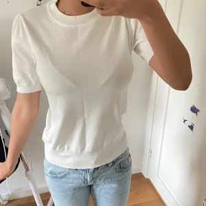 Vit stickad kortärmad tröja - Snygg vit stickad tröja med rund hals och korta ärmar. Tröjan har en mjuk och skön känsla, med lätt puff vid axlarna för en trendig touch. Perfekt att matcha med jeans eller kjol för en clean och fräsch look.