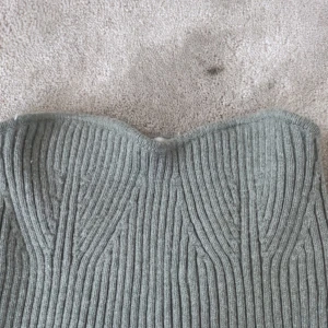 Grå ribbad stickad tubtopp från Zara - Supersnygg grå stickad tubtopp från Zara med ribbad struktur och bandeau-modell. Toppen är ärmlös och har en lätt formad överkant som ger en cool och trendig look. Perfekt att styla med jeans eller kjol för en chill vibe.