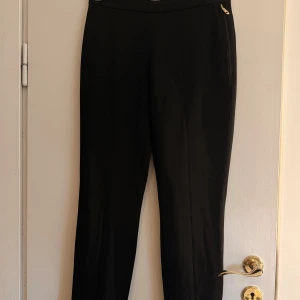 Svarta kostymbyxor J.Lindeberg - Svarta kostymbyxor från J.Lindeberg med smal passform. Byxorna har dragkedjor vid bensluten och en diskret dragkedja i sidan. Snygg minimalistisk look, perfekta till sneakers eller boots. Stängbar slits nertil