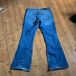 Blå bootcut jeans från Lee - Säljer ett par klassiska blå bootcut jeans från Lee i 100% bomull. Jeansen har normal fair, fem fickor och snyggt utsvängda ben. Perfekta för dig som gillar retrovibbar och vill ha ett par jeans med riktigt skön känsla. 
