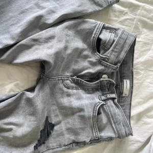 ljusgrå low waist bootcut jeans - Snygga låg midjade grå bootcut jeans med slitna detaljer och råa benslut. Jeansen har svarta trasiga partier på benen för en edgy look. Klassisk femficksmodell och dragkedja i gylfen. Har gjort slitningarna själv och sprätt upp jeansen nera vid fötterna, sjukt snygga men för korta på mig tyvärr