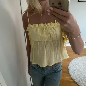 Gul linnetopp från Nelly - Supersöt ljusgul linnetopp från Nelly med smala axelband och volangdetalj upptill. Toppen har knyt i sidorna och en luftig, flowy passform som är perfekt för varma dagar. Materialet är tunt och känns riktigt somrigt. Banden är enkla att gömma, perfekt som tubtopp. Aldrig använd men ingen prislapp kvar