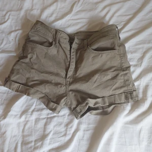 Beige midwaist shorts från &Denim - Snygga beige shorts från &Denim i storlek 34 med midwaist-passform. Klassisk femficksmodell med uppvikta benslut och dragkedja fram. Perfekta för varma dagar och enkla att matcha med din favorit-t-shirt eller hoodie.