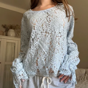 Ljusblå spetsblus neo noir  - Superfin ljusblå blus i spets med blommigt mönster och långa ärmar. Blusen är genombruten och har snygga vågiga kanter både vid ärmslut och nederkant. Perfekt för dig som vill ha en romantisk och trendig look. Aldrig anvönd❤️