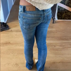 Replay Anbass blå jeans W27 L36 (36) - Säljer ett par Replay Anbass jeans i klassisk blå tvätt med slitningar och snygga detaljer. Modellen har låg midja och smal passform med utsvängda  ben. Jeansen är tillverkade i stretchig bomull och har fem fickor samt dragkedja och knapp framtill.