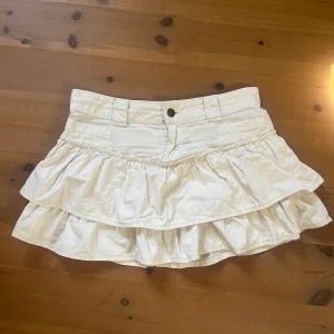 Vit volangkjol - Supersöt vit kortkjol med dubbla volanger från bershka💓 Säljer pga att den var för liten för mig!! Midjemåttet rakt över är 40 cm och längden på kjolen är 32 cm💕 Kjolen har en liten bristning längst fram vi knappen men annars är det inga andra defekter på den🩷