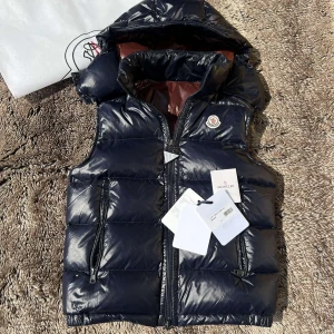 Moncler Bormes Gilet (Navy blå) - Snygg mörkblå dunväst från Moncler i storlek 2/M men passar också S. Den är i otrolig sjuk skick🤩 Det är en väldigt fin vest från Moncler som funkar på Soliga☀️och kyliga dagar🥶. Västens luva är avtagbar med knappar☺️Och den medföljer Moncler Dust bag, och Alla taggarna från butikens köp🙈 sen extra knappar, och Authentic Tringalen🙌❗️ ❗️Priset kan diskuteras❗️obs! Vid snabb affär och bundle köp, men tveka inte att kontakta vid intresse🤭 Frågor om passform och bilder? Kontakta mig gärna🫡
