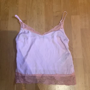 Ljusrosa linnetopp med spets Gina Tricot - Supersöt ljusrosa linnetopp från Gina Tricot i storlek XS. Toppen har tunna axelband och v-ringad hals med spetsdetaljer i rosa både upptill och nedtill. Materialet är mjukt och lätt, perfekt för varma dagar eller när du vill känna dig extra fin.