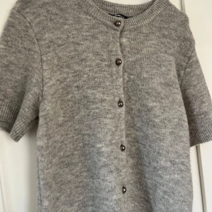 Grå stickad kofta från Gina Tricot - Mysig grå stickad kofta från Gina Tricot med korta ärmar och rund halsringning. Aldrig använd och i storlek L men sitter som s-m