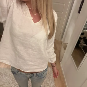 Vit blus i linne från Zara  - Säljer en fräsch vit blus från Zara i mjukt linne. Blusen har långärmade ärmar, v-ringad hals med små knyt och snygga rynkade detaljer upptill. Perfekt till jeans eller kjol för en chill och stilren look.