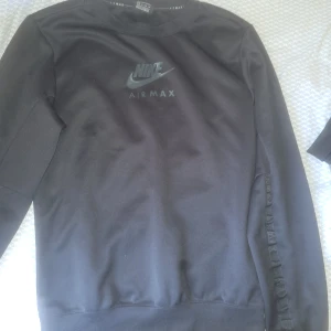 Svarta Nike Air Max mjukisbyxor - Svarta mjukisbyxor från Nike Air Max med logga på benet. Byxorna har snörning i midjan och två stora fickor framtill. Snygg och sportig look, perfekta för chill eller träning. Materialet är mjukt och bekvämt.