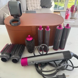 Dyson Airwrap med tillbehör och väska - Säljer en Dyson Airwrap i metallicgrå och rosa med flera stylingtillbehör: rundborste, olika borstar och locktillbehör. Allt kommer med en snygg brun förvaringsväska i läderlook. Perfekt för att fixa håret med olika looks och volym. Funkar jättebra! Som bilderna visar har färgen nötts bort lite lite på vissa ställen