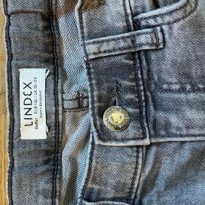 Grå jeansbyxor från Lindex, strl 146 - Snygga grå jeansbyxor från Lindex i klassisk femficksmodell. Byxorna har en cool tvättad look med raka ben och normal passform. Metallknapp framtill och bälteshällor. Perfekt för dig som gillar en chill och stilren vibe.
