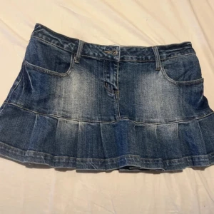 2000s Low waist Denim skirt  - Snygg blå jeanskjol med volangkant nertill och klassiska fickor fram och bak. Kjolen har bälteshällor och stängs med knapp och dragkedja. Perfekt för dig som gillar en avslappnad och trendig stil.