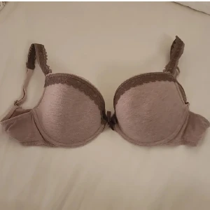 BH - Säljer en söt bh med bruna spetsdetaljer och en liten rosett framtill. Bh:n har justerbara axelband och knäppning bak. Köparen står för frakten 😊