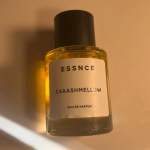 ESSNCE Carashmellow Eau de Parfum - Nästan helt full. Parfymflaska i glas med svart cylinderformad kork och transparent gul vätska. Minimalistisk vit etikett med svart text. Doften heter Carashmellow och är en Eau de Parfum. Perfekt för dig som gillar stilren design och unika doftnoter.