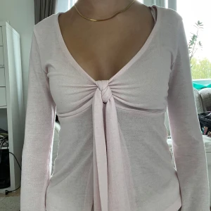 Ljusrosa omlottopp med knyt - Supersöt ljusrosa topp med omlott och knyt framtill. Toppen har lång ärm och är croppad i modellen, med en djup v-ringning. Materialet är mjukt och stretchigt, troligen bomull eller polyester. Perfekt för dig som gillar romantisk och feminin stil. Den har några fläckar, men de syns knappt💖