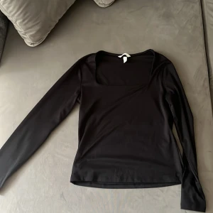 Svart långärmad topp från H&M - Svart långärmad topp från H&M med snygg fyrkantig urringning. Modellen är slim och har en stilren, enkel look som funkar till många olika outfits. Materialet är mjukt och stretchigt, troligen polyester. Perfekt för dig som gillar minimalistisk stil.