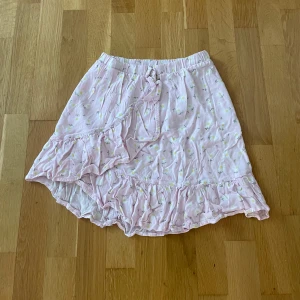 Ljusrosa omlottkjol med volang - Supersöt ljusrosa kortkjol med små blommor, omlottmodell och volangkant. Kjolen har knyt i midjan och är perfekt för en somrig look.