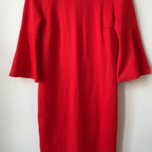 Röd klänning med trumpetärm från Vila - Snygg röd klänning från Vila i storlek S. Modellen är rak med trumpetärmar i trekvarts längd och har en enkel, stilren design utan mönster. Materialet är mjukt och känns som bomull eller polyester. Perfekt för dig som gillar färgstarka plagg med coola detaljer.