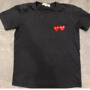 Svart t-shirt från Comme des Garçons - Säljer en svart t-shirt från Comme des Garçons med två röda hjärtan med ögon på bröstet. T-shirten har en klassisk rund hals. Storlek: M dock liten i storleken.