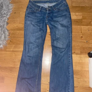 Levi's blå bootcut jeans - Snygga blå jeans från Levi's med klassisk femficksdesign och bootcut-ben. Jeansen har låg midja och är gjorda i slitstarkt denim med coola slitningar framtill. Perfekt passform och ikonisk Levi's-detalj på bakfickan. Passar dig som gillar en avslappnad och trendig look.