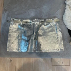 Silvrig kortkjol med bälte - Säljer en glansig silvrig kortkjol med tillhörande bälte. 