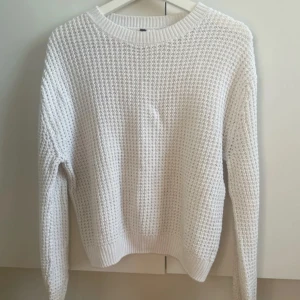 Vit stickad tröja med grov struktur - Säljer en vit stickad tröja med grov, strukturerad yta och breda ribbade muddar vid ärmslut och hals. Tröjan har en klassisk rund halsringning och långärmade ärmar. Perfekt för dig som gillar en enkel men snygg stil. Ärmarna e lite slitna och missfärgade. Köpt secondhand 