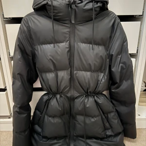 Svart pufferjacka från Rains - Aldrig använd! Inre dragkedja har gått sönder (går att fixa). Nypris: 3999kr