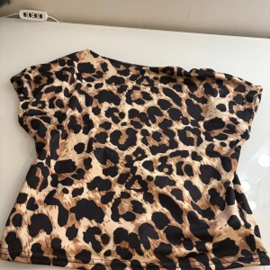 Leopardmönstrad croppad topp - Snygg croppad topp med leopardmönster i beige och svart. Toppen har korta ärmar och är tillverkad i ett mjukt och stretchigt syntetmaterial som sitter skönt mot kroppen. Perfekt för dig som vill sticka ut med ett djuriskt print och cool vibe.