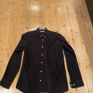 Svart skjorta från Premium by Jack & Jones - Stilren svart skjorta från Premium by Jack & Jones med klassisk krage och vita knappar. Skjortan har lång ärm, bröstficka och en rak passform. Perfekt för dig som gillar enkel och snygg design. Materialet känns mjukt och är troligtvis bomull. priset kan diskuteras