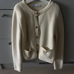 Beige stickad kofta från Zara - Snygg beige stickad kofta från Zara med guldfärgade knappar framtill och på fickorna. Koftan har rund hals, två fickor och långa ärmar. Perfekt för lager-på-lager och chill stil under höst och vinter. Materialet är mjukt och ger en cozy vibe. Stilig men bekväm kofta, gossipgirl vibe🤍