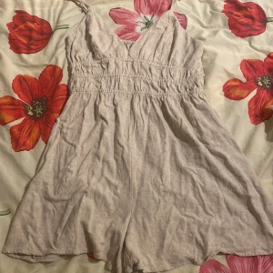 Beige linne-shorts från FB Sister S - Säljer ett par ljusbeige shorts från FB Sister i storlek S. De har hög midja med smock och breda ben, tillverkade i mjukt linnematerial. Perfekta för varma sommardagar och har en enkel, clean look med v-ringad överdel och tunna axelband.