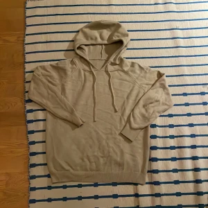 Beige stickad hoodie med huva - Snygg beige stickad hoodie med huva och snörning. Tröjan har lång ärm och ribbade muddar vid ärmslut och nederkant. Perfekt för dig som gillar en chill och enkel stil. Materialet är mjukt och skönt mot huden.
