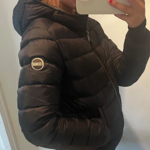 Svart Colmar pufferjacka med huva - Svart dunjacka från Colmar Originals med huva och dragkedja framtill. Jackan har quiltad design, långärmade ärmar och logotyp på ärmen⚡️Storlek 40 i franska mått vilket är xs💓