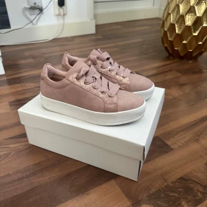 Rosa sneakers med glitterdetaljer - Snygga rosa sneakers med breda matchande snören och glittriga detaljer på sidorna och hälen. Skorna har en vit platt sula och rund tå. Materialet är mockaliknande med inslag av syntet på glitterpartierna. Perfekt för dig som vill ha en cool och feminin stil.
