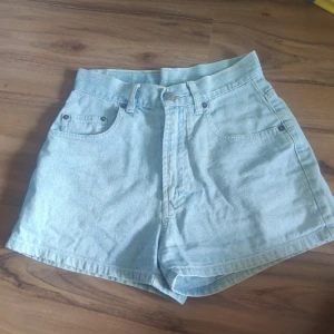 Ljusblå högmidjade jeansshorts Esprit - Snygga ljusblå jeansshorts från Esprit med hög midja och klassisk femficksdesign. Shortsen har bälteshällor, knapp och dragkedja framtill samt coola nitar vid fickorna. Perfekta för sommarens alla häng och chill dagar.