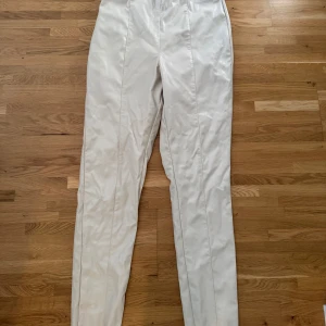 Vita raka kostymbyxor - Snygga vita kostymbyxor med rak passform och pressveck längs benen. Byxorna har hög midja och är tillverkade i ett slätt material som ger en clean och fräsch look. Perfekta att styla med en cool t-shirt eller skjorta för en trendig vibe.