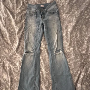 Bootcut jeans med slitna knän från Nelly - Bootcut jeans från Nelly i ljusblå tvätt med låg midja och coola slitningar över båda knäna. Baktill finns två fickor med lock och knapp. Jeansen har klassisk femficksdesign och är gjorda i mjukt denimtyg. Perfekt för dig som gillar retrovibe och avslappnad stil. Är i storlek EU 36 men dem är uppsydda så dem passar än med 73cm i innnerbens längd